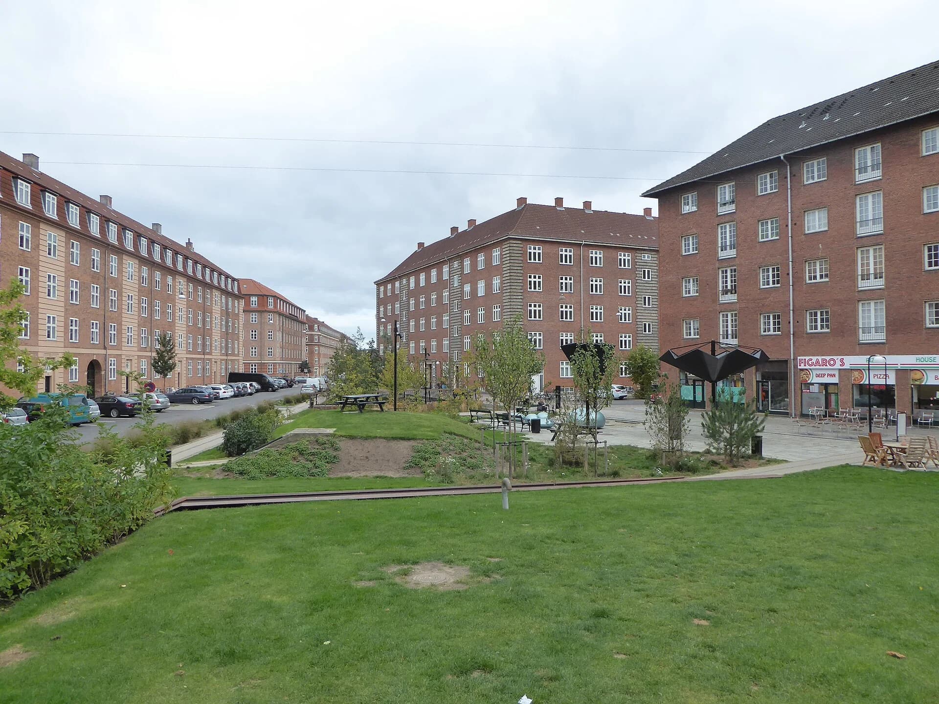 Tåsinge Plads in Østerbro, Copenhagen: a former street converted into a square of lawns, low planted mounds, young trees and a channel, surrounded by five-storey brick apartment blocks.