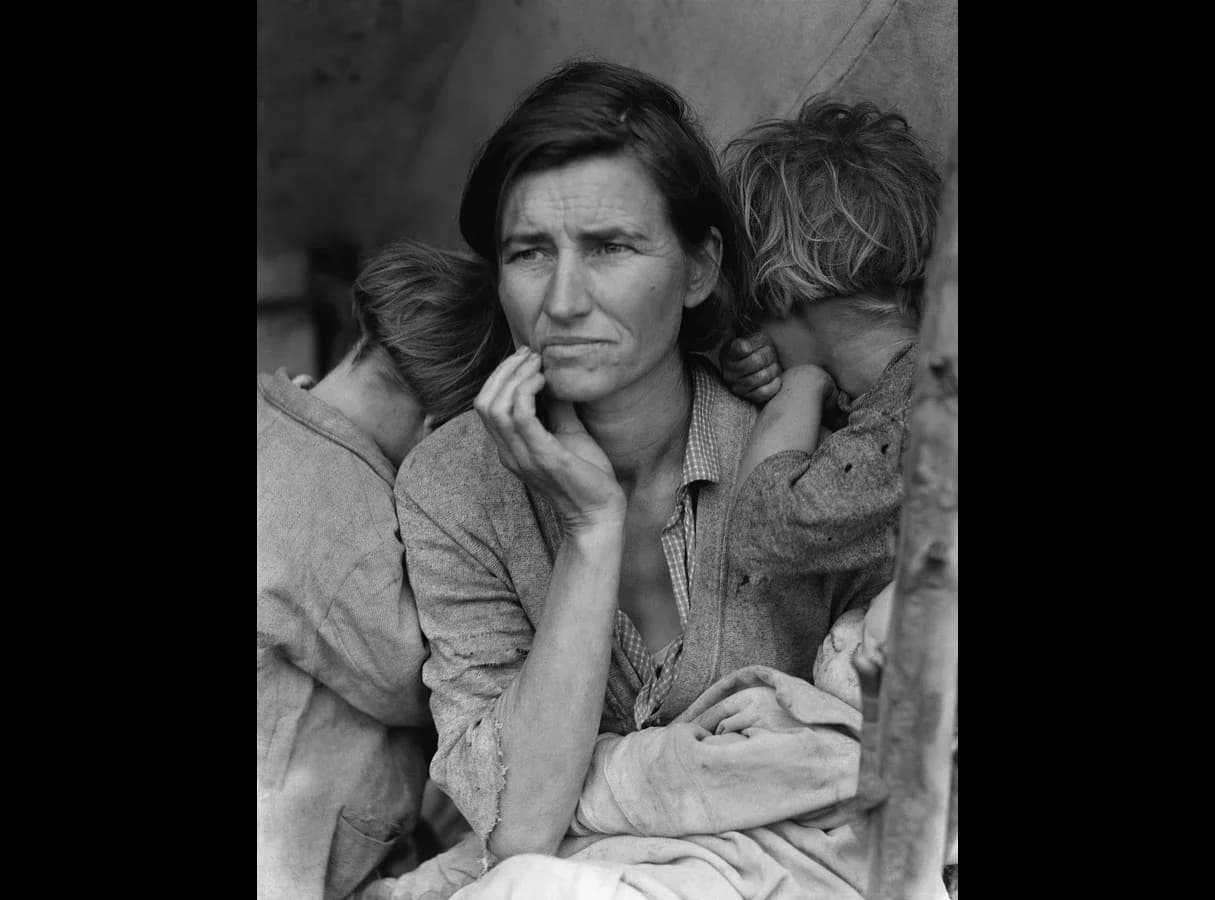 Black-and-white photograph of a worried woman in worn clothes, her hand raised to her chin, with two children leaning on her shoulders, faces turned away, and a baby on her lap.