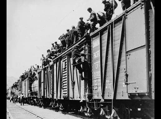 Black-and-white photograph of a crowd of men in caps and work clothes standing on and beside the roofs of railway boxcars.