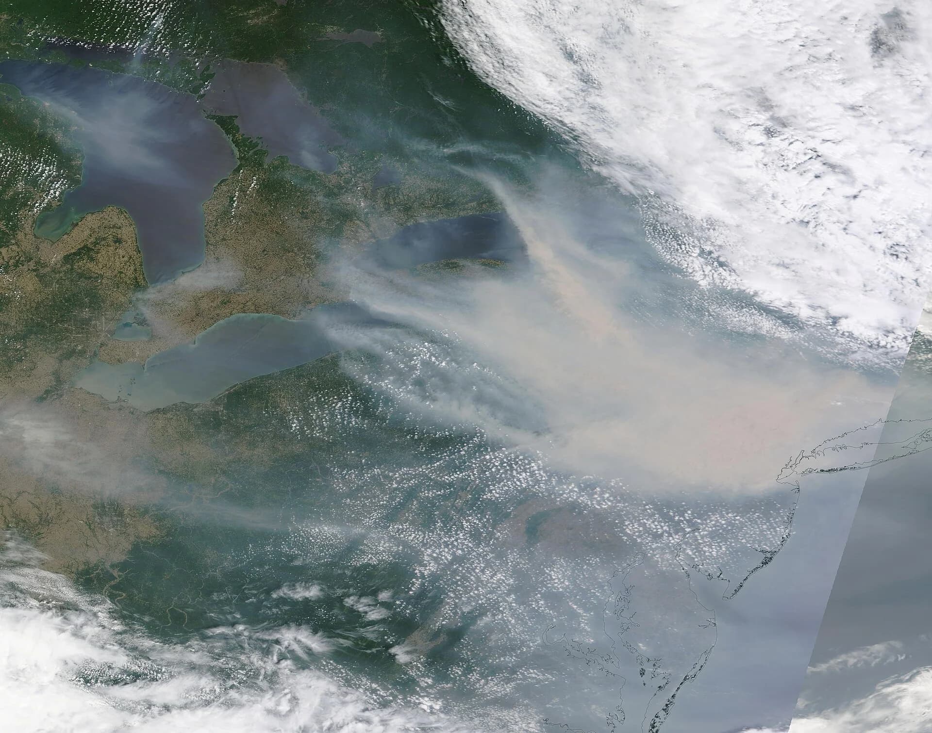 Satellite image on 7 June 2023: a thick grey-brown smoke plume from wildfires in Quebec spreading south over the Great Lakes region and the north-eastern United States to the Atlantic coast near New York.
