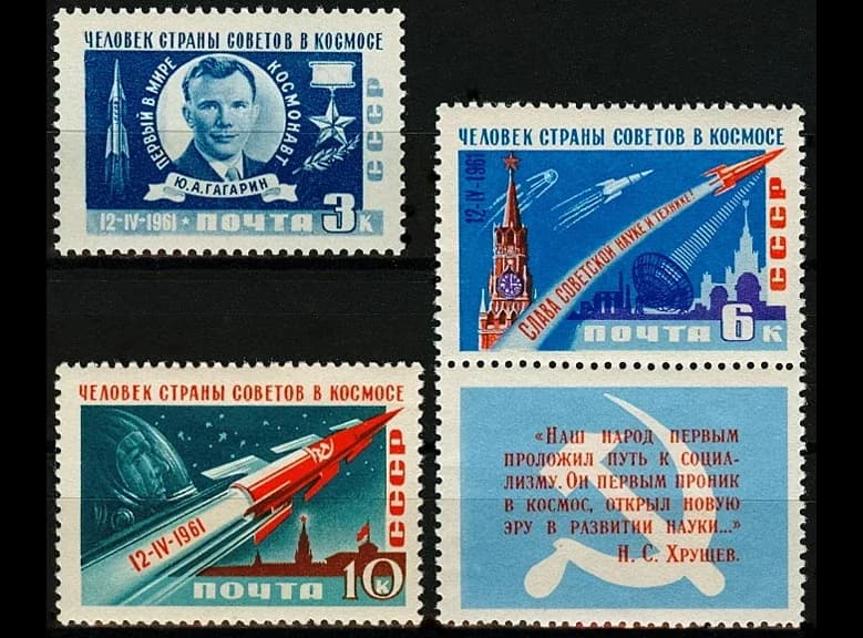 Three Soviet postage stamps of April 1961 headed “A man of the Soviet country in space”: Gagarin’s portrait, a rocket rising past the Kremlin, and a red rocket with Gagarin in a helmet. A blue label beside them carries a quotation from Khrushchev under a hammer and sickle.