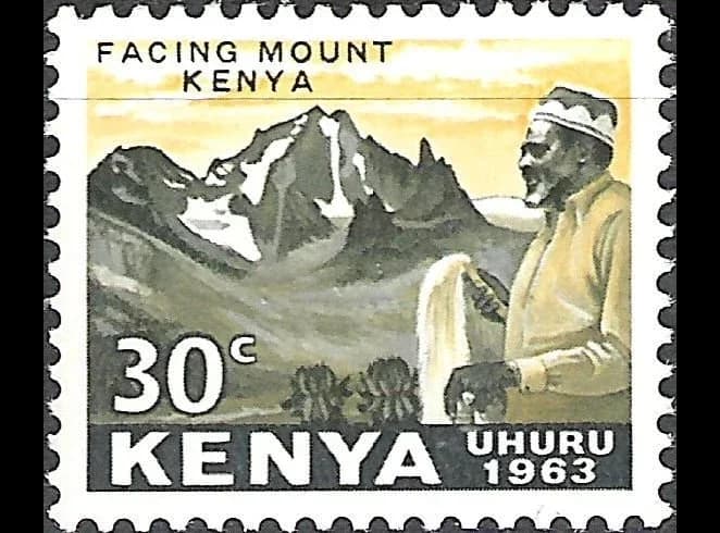 A Kenyan postage stamp of 1963 worth 30 cents. Jomo Kenyatta, wearing a cap and holding a fly whisk, looks towards the snow-capped peaks of Mount Kenya. The stamp reads “Facing Mount Kenya”, “Kenya” and “Uhuru 1963”.