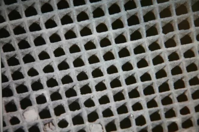 Close-up photograph of the ceramic core of a catalytic converter: a grid of many small square channels whose walls are coated with a grey-white washcoat.