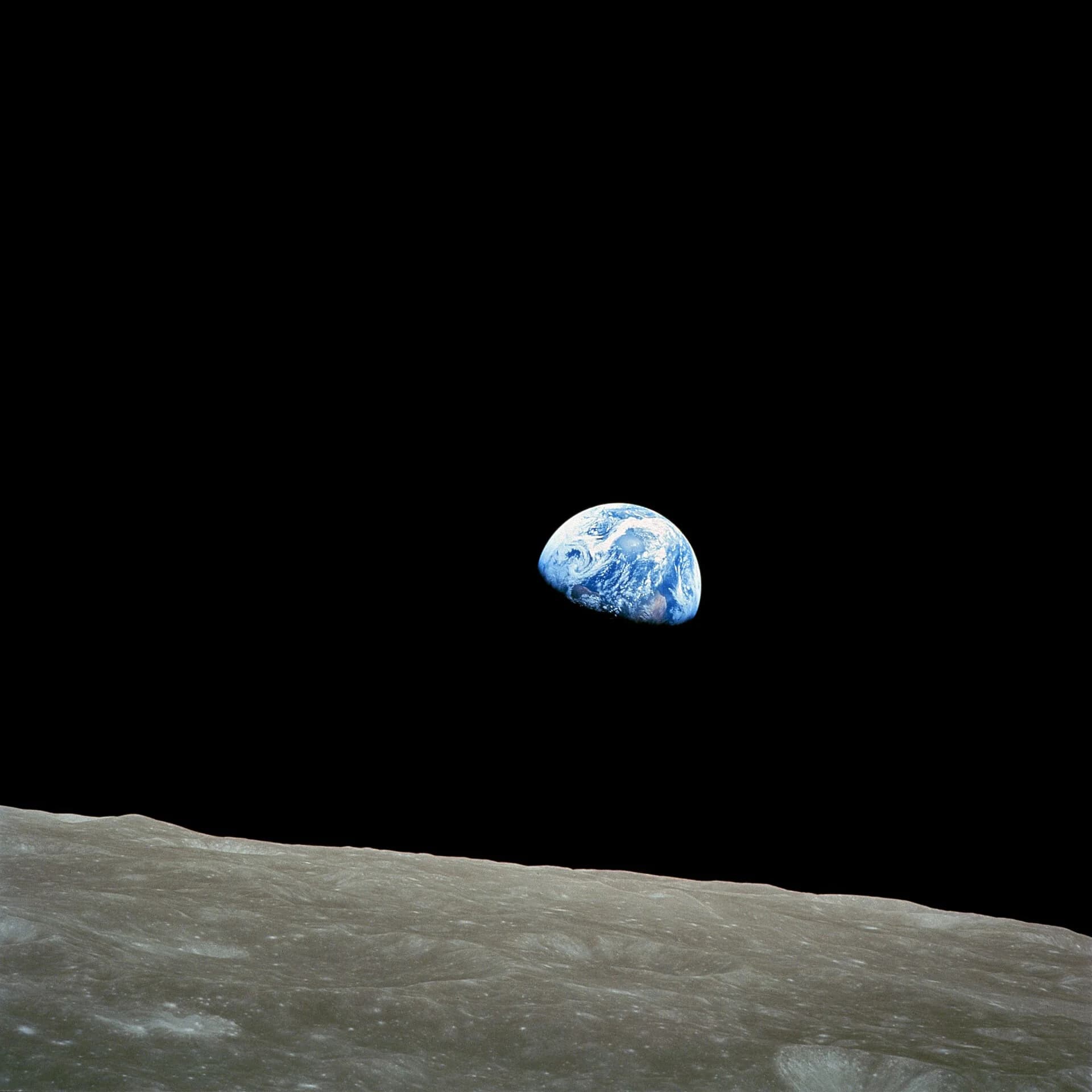 The Earth, half lit, rising above the grey, cratered horizon of the Moon against a black sky, photographed from lunar orbit by the Apollo 8 crew.