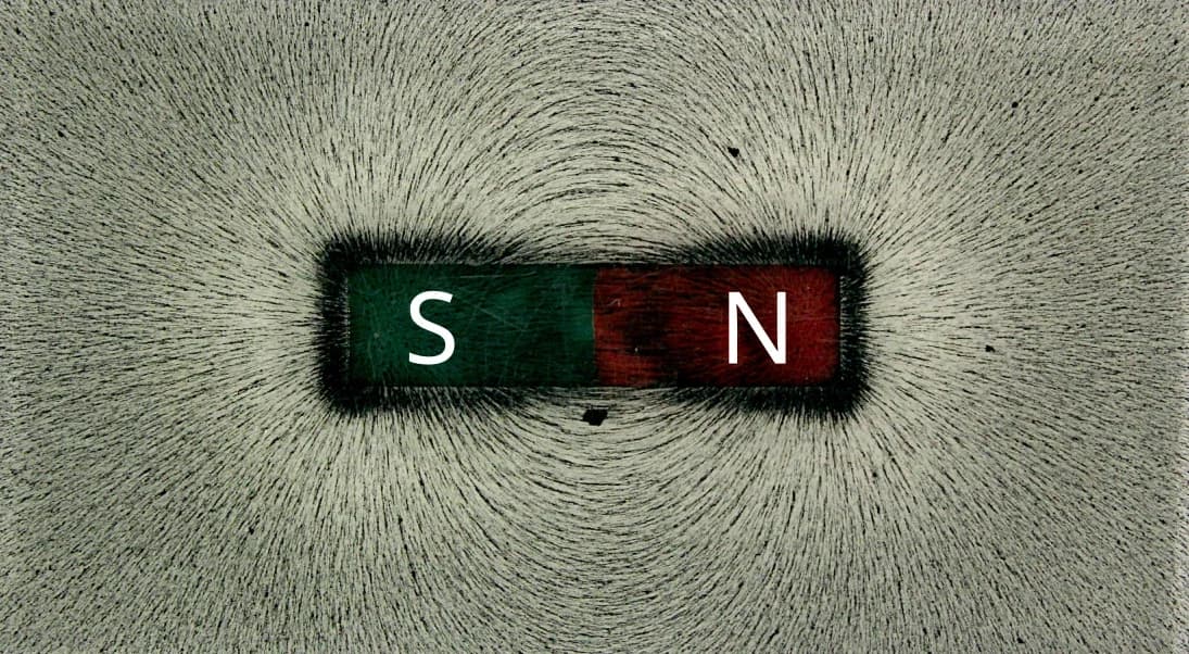 Photograph of iron filings sprinkled on a sheet over a bar magnet. The filings line up in curved lines that leave one end of the magnet and loop round to the other end, crowding together near the two poles.