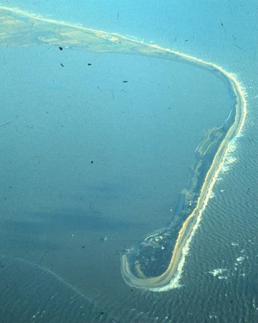 Aerial photograph of Spurn, a long, narrow curved spit of sand and shingle extending across the mouth of the Humber Estuary, with the open North Sea on one side and the sheltered estuary on the other.