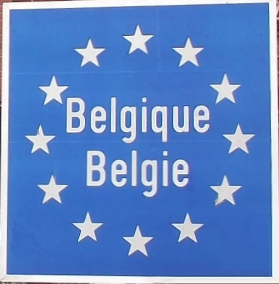 A blue road sign ringed with twelve yellow EU stars reading Belgique and Belgie, marking an open border crossing into Belgium with no checkpoint.