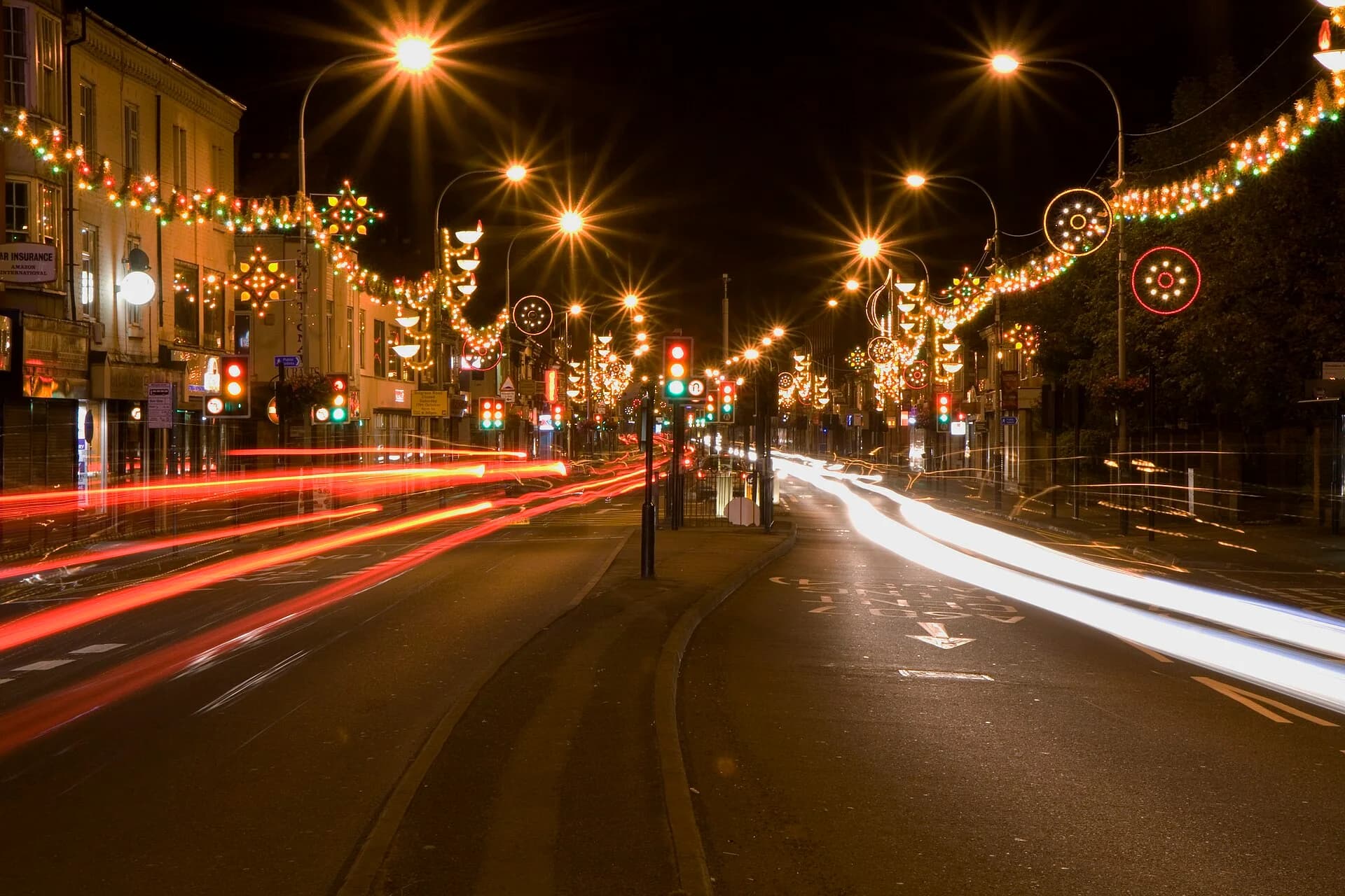 Belgrave Road, Leicester, at night during Diwali 2009: strings of festive lights and illuminated lamps and stars hang across the street above shops, traffic light trails below.