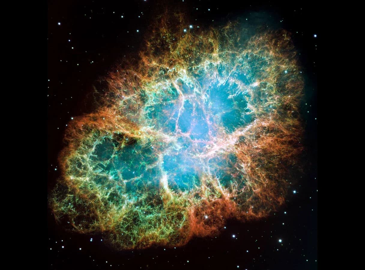 The Crab Nebula photographed by the Hubble Space Telescope: an oval cloud with tangled orange and red filaments around a glowing blue-white centre.