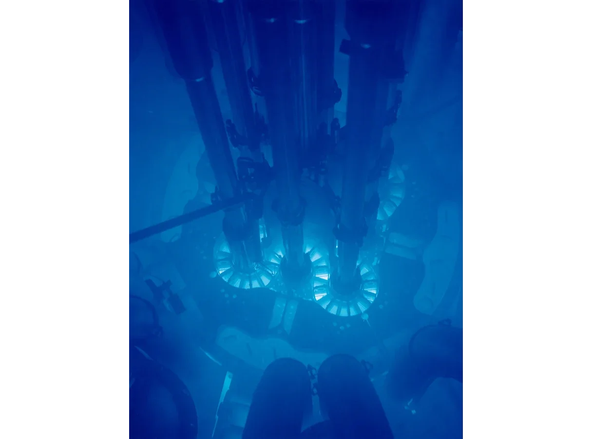 Looking down through deep water into the core of the Advanced Test Reactor at Idaho National Laboratory. The core glows bright blue and is surrounded by dark water and metal structures.