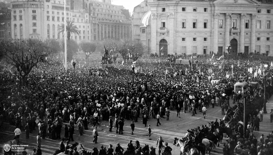 Black-and-white photograph of a huge crowd filling the Plaza de Mayo in Buenos Aires, carrying flags and banners, with mounted police in the foreground and large public buildings behind.