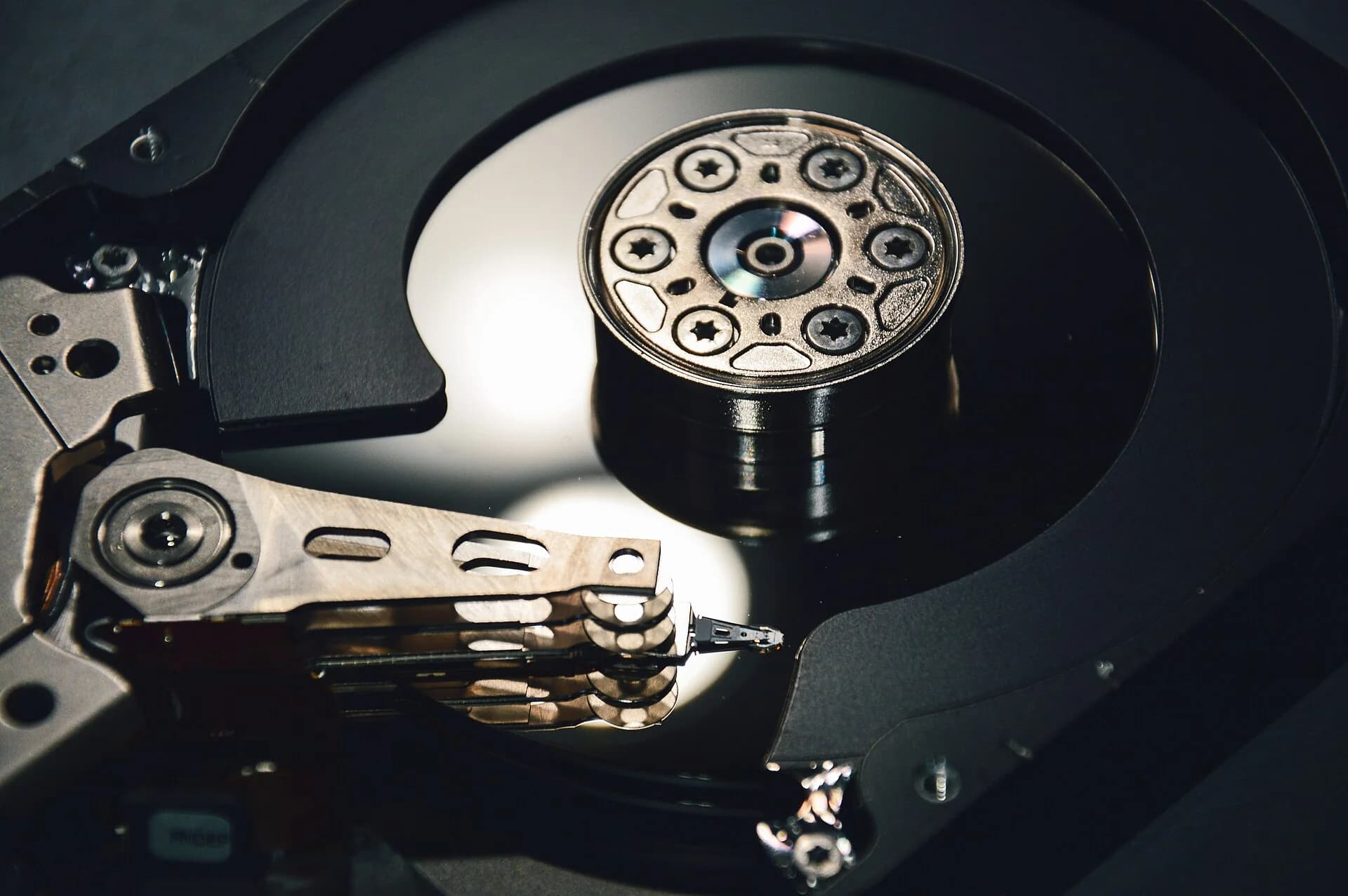 Close-up photo of an opened hard disk drive: a shiny platter on a central spindle, with the actuator arm and its read/write heads reaching across the platter surface.