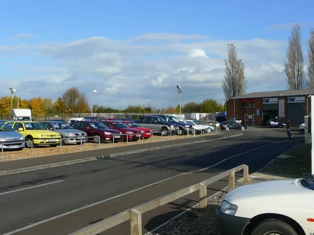 A used-car dealer's forecourt in England, with rows of second-hand cars parked in front of a showroom.