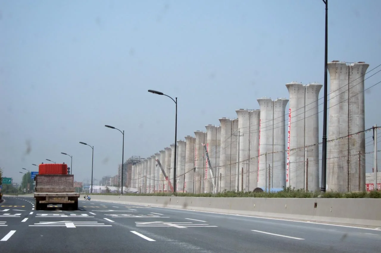 A row of tall concrete piers for an elevated high-speed railway under construction beside a multi-lane highway near Hangzhou, China, in 2010, with a lorry on the road.