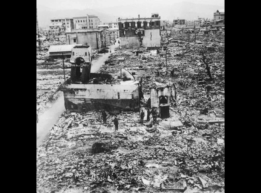 Black-and-white photograph of Hiroshima in ruins: rubble covers the ground between a few gutted concrete buildings, and several men stand among the debris.