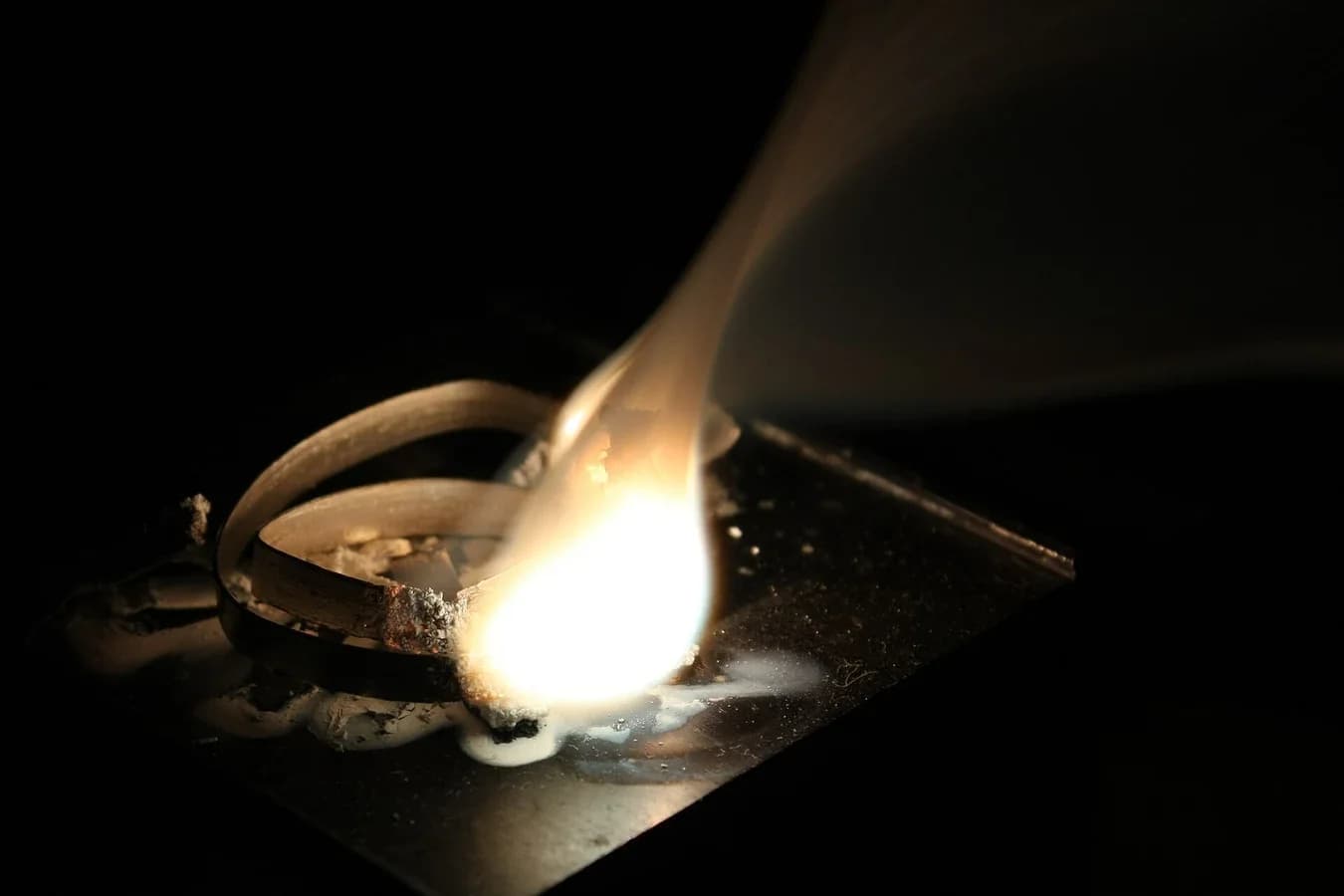 Photograph of a strip of magnesium ribbon burning with an intensely bright white flame and white smoke of magnesium oxide.