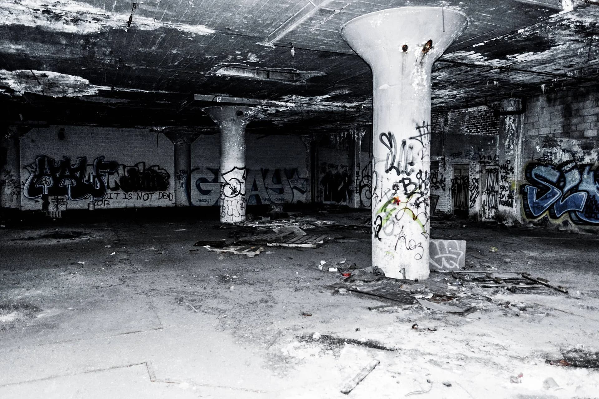 Interior of the abandoned Packard car plant in Detroit: a large empty factory floor with concrete pillars, broken ceilings, debris and graffiti, including the words 'Detroit is not dead'.
