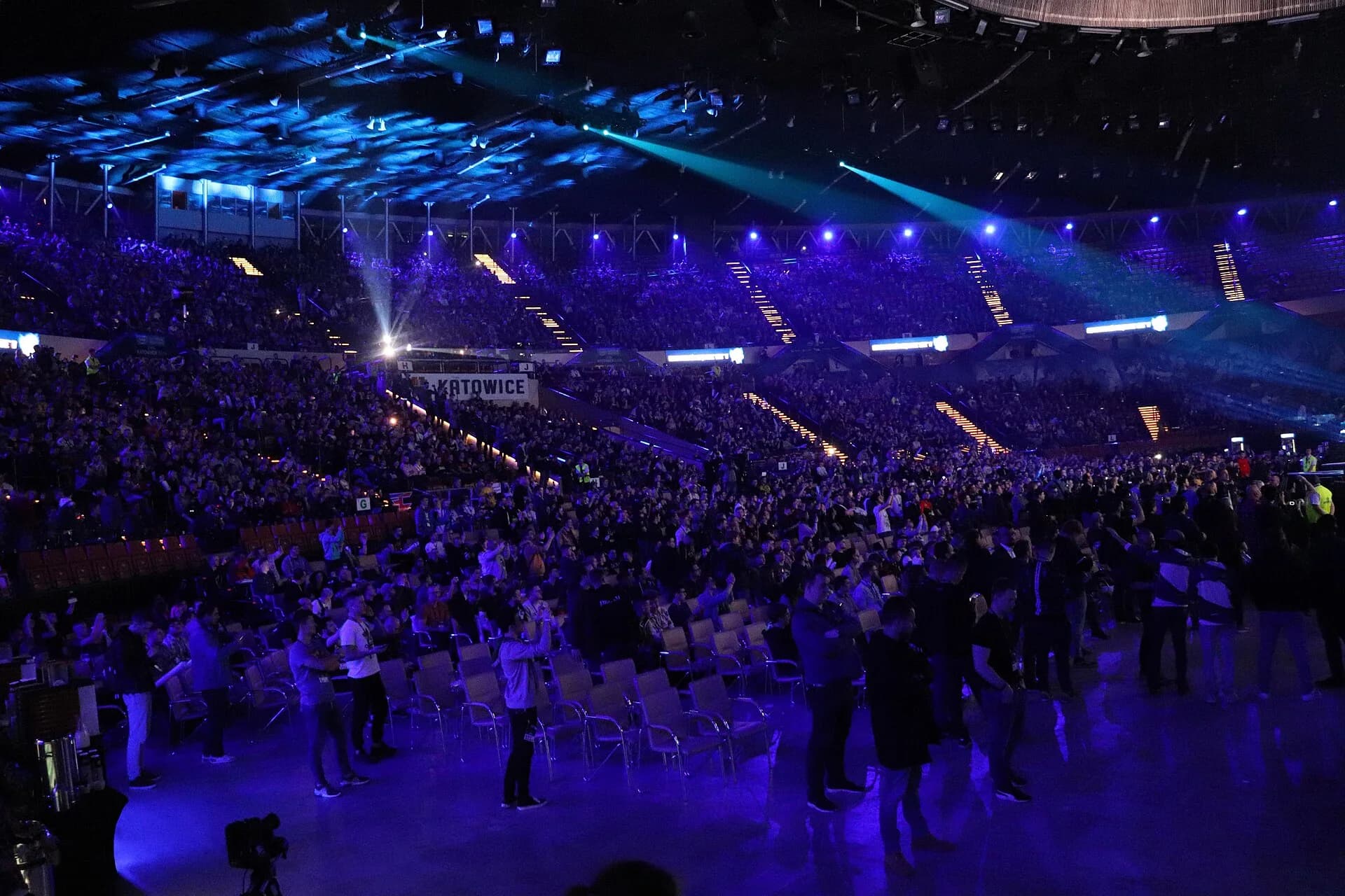 A packed arena lit in blue, with thousands of spectators in tiered seats and on the floor watching the IEM Katowice Major 2019 Counter-Strike tournament in the Spodek arena, Poland.