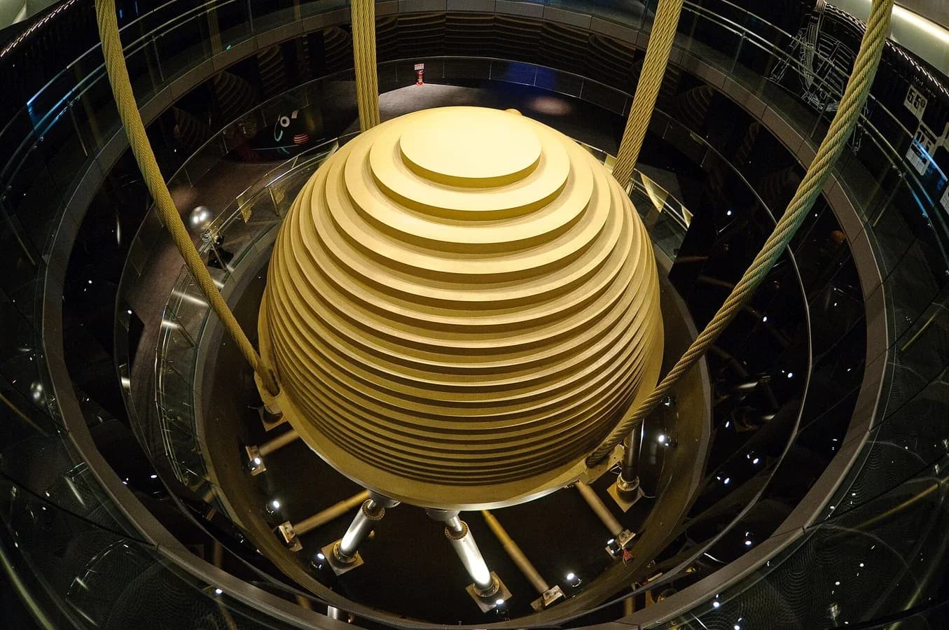 A huge gold-coloured steel sphere suspended by cables inside the upper floors of the Taipei 101 skyscraper, with hydraulic dampers attached below it.