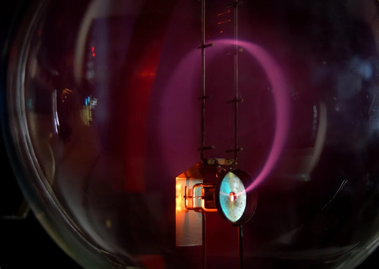 A glass bulb in the dark containing a glowing violet circle: a beam of electrons leaving an electron gun at the bottom right and bent into a circle by a magnetic field.